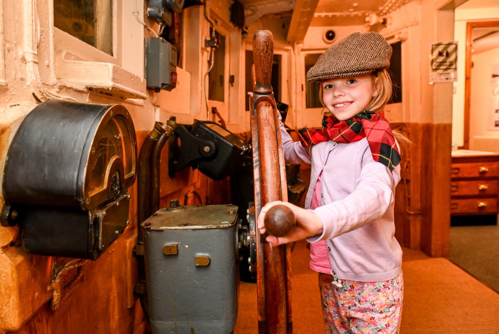 A young girl holds the wheel in the The Wheelhouse inside the main attraction at Grimsby Fishing Heritage